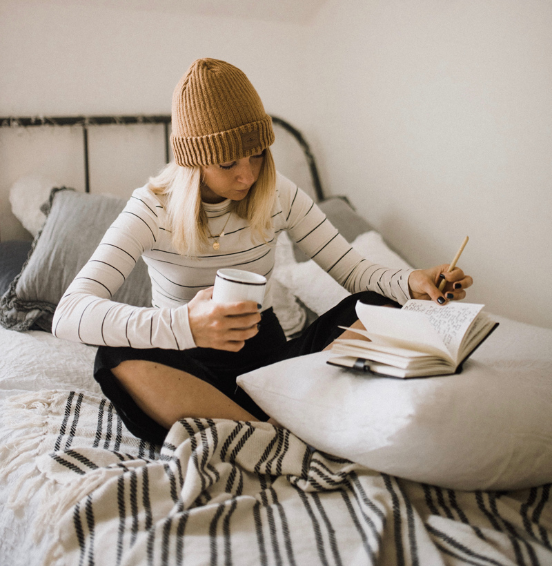 12 Ways to Add More Joy to Your Book-Reading Bliss, woman in hat, journaling on bed while holding coffee